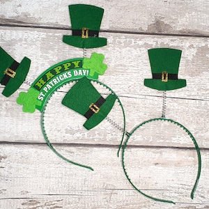 May include: Three green felt leprechaun hats on headbands with a spring attached to the top of each hat. The headband with the hat in the centre has a green banner that says "Happy St. Patricks Day!"