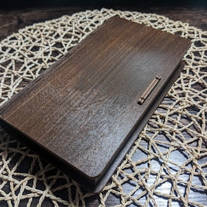 Puede incluir: Una caja de madera marrón oscuro con un cierre de metal. La caja está sobre una estera de paja tejida.