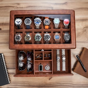 May include: A brown leather watch display case with a glass top, showcasing twelve watches with various band colors and face designs. The open drawer reveals sunglasses, jewelry, and watch straps. The case sits on a wooden surface.
