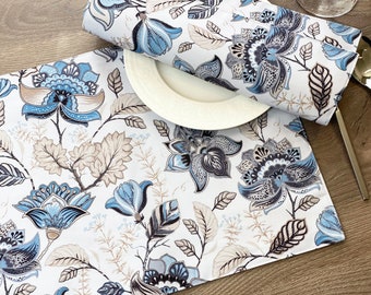 May include: A white table runner with a blue and brown floral pattern. The runner features a repeating design of stylized flowers and leaves.