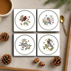 May include: Four square white ceramic coasters with botanical bird illustrations. Each coaster features a different bird design, surrounded by a green leaf border. Butterflies and floral elements are also included in the designs.