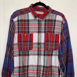 May include: A long-sleeved plaid shirt in red, green, white, and blue. The shirt has two front pockets and wooden buttons. The collar and cuffs are red. The brand name "ROO CROSSING" is visible on the collar.