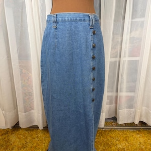 May include: A light blue denim skirt with a button-up front. The skirt is a midi length and has a classic, vintage style. The skirt is displayed on a mannequin.