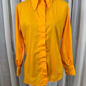 May include: A white ceramic mug with a black handle and the text "But First, Coffee" in a bold, black font. The mug is set against a blurred background, highlighting its clean design.