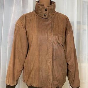May include: A brown leather bomber jacket with a high collar and a zipper closure. The jacket has a ribbed knit collar, cuffs, and waistband.