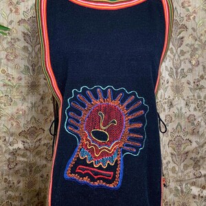 May include: Black sleeveless knitted top with a colorful embroidered design of a stylized face. The top has a multi-colored trim around the neckline and hem.
