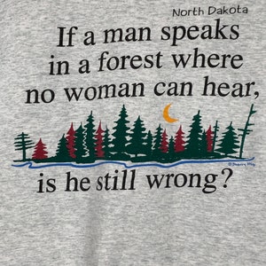 May include: A gray t-shirt with a black and green forest scene and the text "North Dakota If a man speaks in a forest where no woman can hear, is he still wrong?"