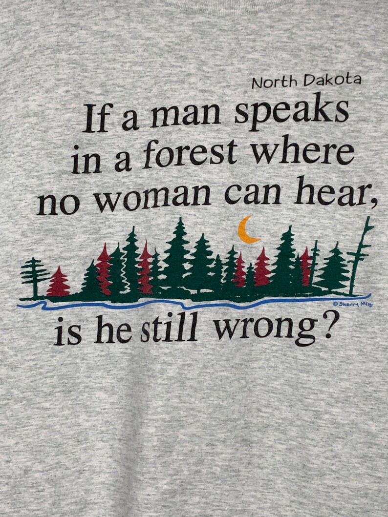May include: A gray t-shirt with a black and green forest scene and the text "North Dakota If a man speaks in a forest where no woman can hear, is he still wrong?"