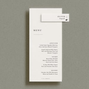 May include: A tall, rectangular white menu card with black serif text listing appetizers, entrees, and desserts. A smaller white rectangular name card with the text OLIVER Fitzgerald and a small black sheep icon is attached to the top right.