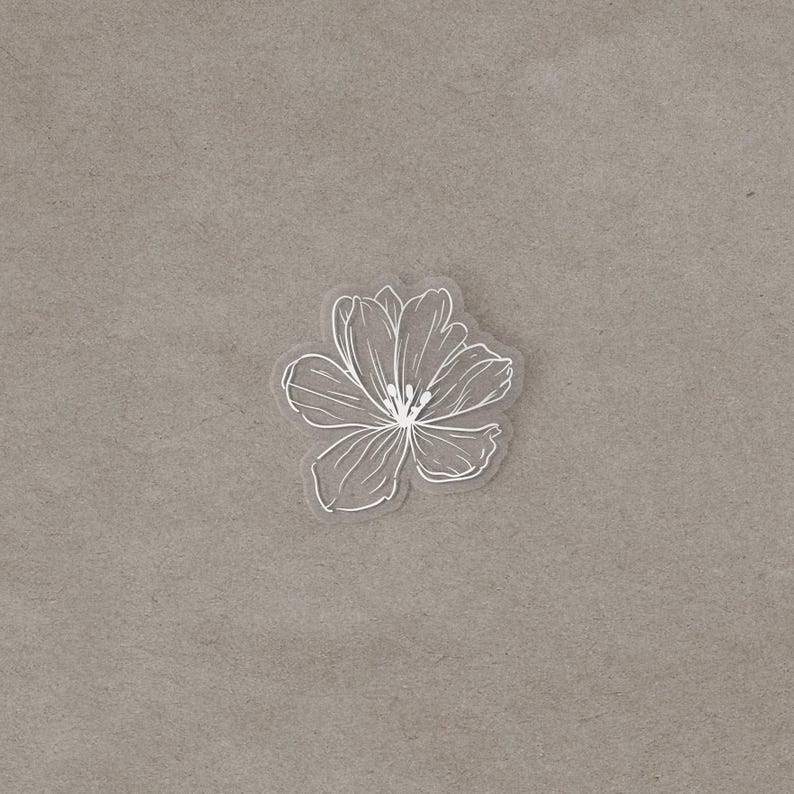A transparent vinyl sticker with a white line drawing of a flower centered on a textured gray background.