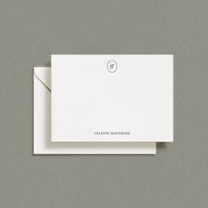 A white flat notecard resting on top of a matching envelope against a gray textured surface.