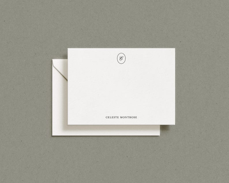 A white flat notecard resting on top of a matching envelope against a gray textured surface.