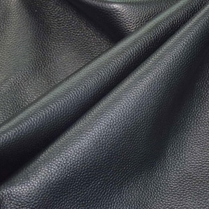 May include: Close-up of a dark navy blue leather material with a textured, pebbled surface. The leather is draped in soft folds, creating shadows and highlights that emphasize its supple texture. The overall appearance suggests a high-quality material.