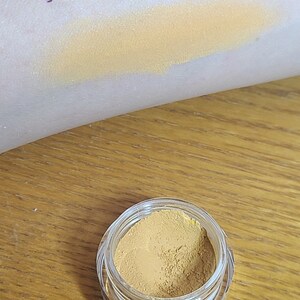 Puede incluir: Un peque&ntilde;o tarro de sombra de ojos de color amarillo dorado con la palabra "waffle" escrita en morado en el brazo de una persona.