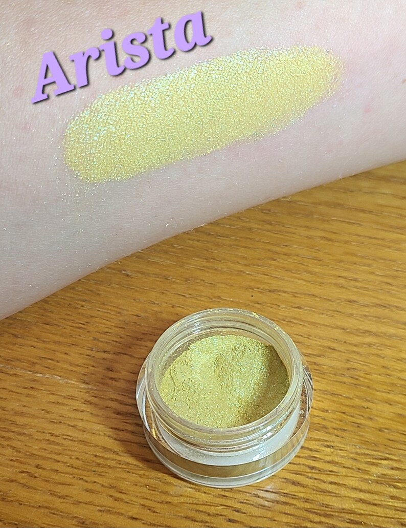 Puede incluir: Arista es el nombre de esta sombra de ojos amarilla con un acabado brillante. La sombra de ojos est&aacute; en un peque&ntilde;o frasco redondo con una tapa transparente.