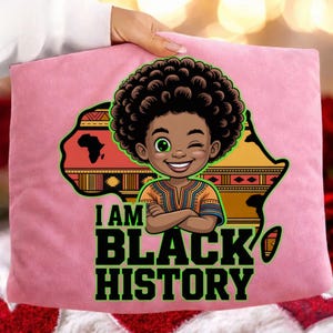 Peut inclure: Coussin rose avec une illustration de dessin anim&eacute; d'un enfant noir qui fait un clin d'&oelig;il avec une afro, sur une carte de l'Afrique. Le texte "I AM BLACK HISTORY" est imprim&eacute; en vert.
