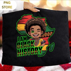 Peut inclure: Coussin noir avec un dessin anim&eacute; d'un enfant souriant devant un contour du continent africain aux couleurs du drapeau. Le texte "I AM BLACK HISTORY" est en vert et noir. Le coussin est tenu par une personne.