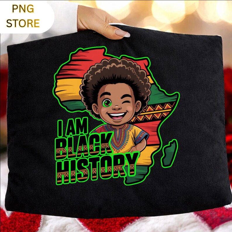 Peut inclure: Coussin noir avec un dessin anim&eacute; d'un enfant souriant devant un contour du continent africain aux couleurs du drapeau. Le texte "I AM BLACK HISTORY" est en vert et noir. Le coussin est tenu par une personne.