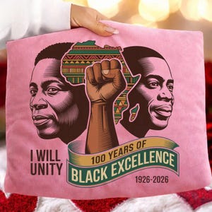 May include: Pink cushion featuring a graphic celebrating Black excellence. The design includes two portraits of Black men, a raised fist, and an outline of Africa. Text reads "I Will Unity" and "100 Years of Black Excellence 1926-2026."