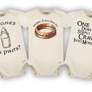 May include: Three cream-colored baby onesies with black text and illustrations. One says "It comes in pints?" with a bottle illustration. Another says "One baby to rule them all" with a ring illustration. The third says "One does not simply crawl into Mordor."