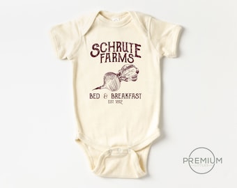 May include: A cream-colored baby onesie with a brown graphic of a beet and the text "Schrute Farms Bed & Breakfast Est 1812".
