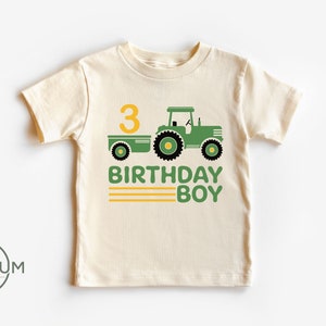 May include: A light beige t-shirt with a green tractor and trailer, a yellow number 3, and the text "3 Birthday Boy" in green and yellow.
