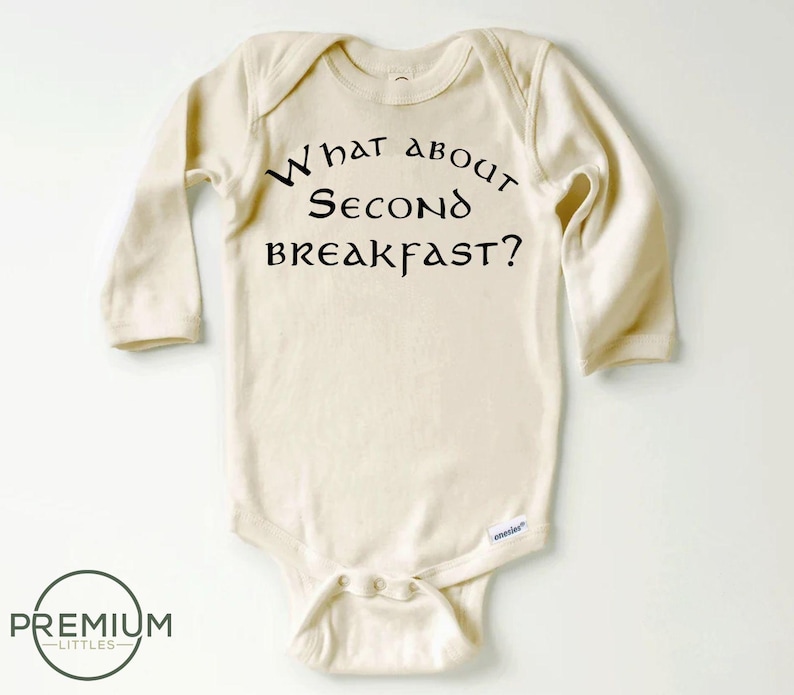 May include: A cream-coloured long-sleeved baby onesie with the text "What about second breakfast?" printed in black.