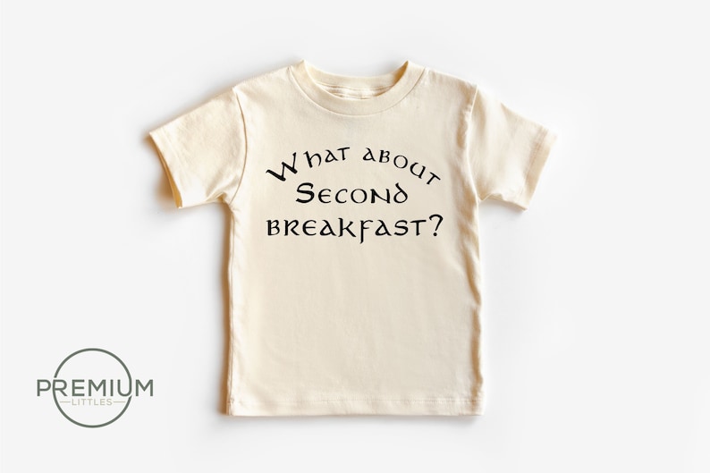 May include: A cream coloured short-sleeved t-shirt with the text "What about Second Breakfast?" printed in black.