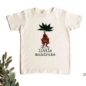 May include: A cream colored t-shirt with a cartoon illustration of a mandrake plant with the text "little mandrake" printed below the image.