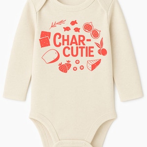 May include: Cream-colored baby bodysuit with long sleeves. The front features a red graphic of the words "CHAR-CUTIE" surrounded by illustrations of crackers, cheese, strawberries, figs, and olives. A cute and playful design for a baby.