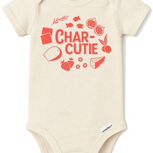 May include: Cream-colored baby onesie with short sleeves. The front features the red text "CHAR-CUTIE" with illustrations of crackers, fish, figs, cheese, strawberries, and other food items. The onesie has a snap closure.