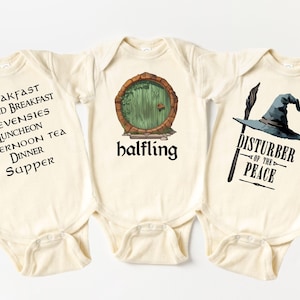 May include: Three cream-colored baby onesies with black text and illustrations. One says "BREAKFAST, SECOND BREAKFAST, ELEVENSIES, LUNCHEON, AFTERNOON TEA, DINNER, SUPPER." Another has a green door and the word "halfling." The third says "DISTURBER OF THE PEACE."