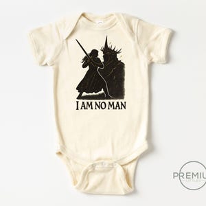 May include: Cream-colored baby bodysuit with a black graphic of a figure wielding a sword facing a dark silhouette. The text "I AM NO MAN" is printed below the figures. A round logo is in the bottom right corner.