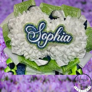 May include: A decorative wreath featuring white floral elements and lime green mesh ribbon accents. Centered is a dark blue and white patch with the name Sophia in a cursive script font, outlined in a lime green border against the white flowers.