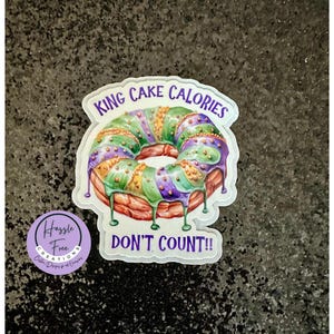 May include: A white sticker with a purple and green donut with the text "King Cake Calories Don't Count!" and a small purple sticker with the text "Hassle Free Creations".