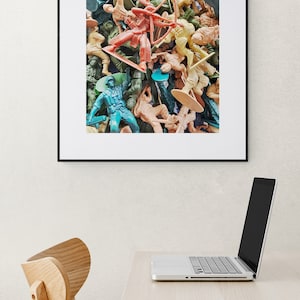 May include: A framed print featuring a dense collection of plastic toy soldiers in various colors, including green, tan, and red. The figures are arranged in a chaotic, overlapping manner, creating a textured visual effect.