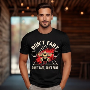 May include: Black t-shirt with a red and white graphic of a person lifting weights. The graphic says "Don't fart, don't fart" and "Don't fart" in a triangle shape.