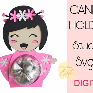 May include: Pink and white candy holder shaped like a Japanese girl with flowers in her hair. The holder has a clear plastic circle in the center to hold candy. The text "CANDY HOLDER Studio Svg DIGITAL" is on the right side of the image.