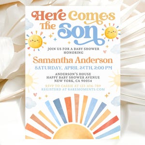 Pode incluir: Um convite para chá de bebé com o texto "Here Comes The Son" em laranja e azul. O convite inclui o nome da homenageada, data, hora e local, juntamente com informações de RSVP. O design apresenta sóis, nuvens e um arco-íris.