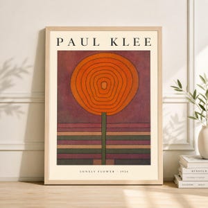 May include: Framed art print of Paul Klee's "Lonely Flower - 1934." The artwork features a large orange flower with concentric circles on a dark red background. The stem is green, and the base has horizontal stripes of various colors. The print is in a light wood frame.