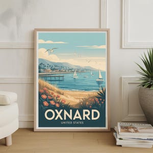 May include: Framed art print featuring a coastal scene with sailboats on the water, a pier, and the text "OXNARD UNITED STATES". The artwork has a vintage travel poster style with a blue, beige, and green color palette.