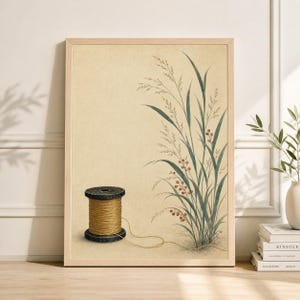 Op de afbeelding: Een ingelijste kunstdruk met een vintage illustratie. De afbeelding toont een garenklos en hoog gras met rode bessen. Het kleurenpalet omvat beige, bruin, groen en rood. De print zit in een licht houten frame.