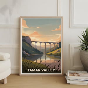 Puede incluir: Lámina enmarcada con un paisaje del valle del Tamar. La obra representa un puente de piedra sobre un río tranquilo, con colinas verdes y un cielo al atardecer. El texto "_ TAMAR VALLEY _" está en la parte inferior.