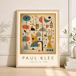 May include: Framed art print featuring an abstract design with geometric shapes in orange, teal, yellow, and black. The print includes the text "PAUL KLEE" and "PARK BEI LU - 1938" in a light beige frame. The artwork is displayed on a wooden surface.