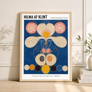 Puede incluir: Impresión artística enmarcada con un diseño abstracto colorido de Hilma af Klint. La obra de arte tiene un fondo azul con formas circulares blancas, rosas, amarillas y negras. El texto "HILMA AF KLINT" y "PIONJÄR FÖR ABSTRAKT KONST" está en la parte superior. El título "Group IV, The Ten Largest, No. 1, Childhood" está en la parte inferior.