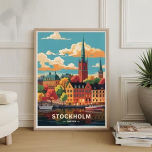 May include: A framed art print featuring a colorful illustration of Stockholm, Sweden. The artwork depicts buildings, boats, and a church with a tall spire, set against a blue sky with orange and white clouds. The word "STOCKHOLM" is printed at the bottom.