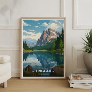 Könnte beinhalten: Gerahmter Kunstdruck mit einer Landschaft des Triglav-Nationalparks. Das Kunstwerk zeigt eine Bergkette, die sich in einem See spiegelt, unter einem blauen Himmel mit Wolken. Der Druck hat einen hellen Holzrahmen und den Text "TRIGLAV - NATIONAL PARK".