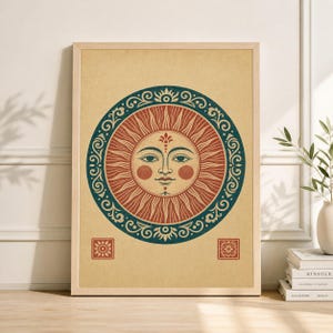 May include: A framed print featuring a stylized sun with a face, radiating red rays, and a blue decorative border. The sun is centered on a beige background, with small square designs in the corners. The artwork is in a wooden frame.