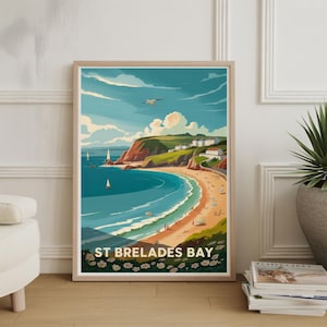 May include: A framed print depicting St Brelades Bay, a coastal scene with a sandy beach, turquoise water, and green cliffs. The artwork is in a vintage travel poster style, with sailboats, clouds, and the text "ST BRELADES BAY" at the bottom.