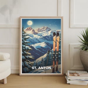 May include: A framed print featuring a winter landscape with snow-covered mountains under a moonlit sky. Two pairs of skis and poles stand in the foreground. The print includes the text "ST. ANTON - AUSTRIA".